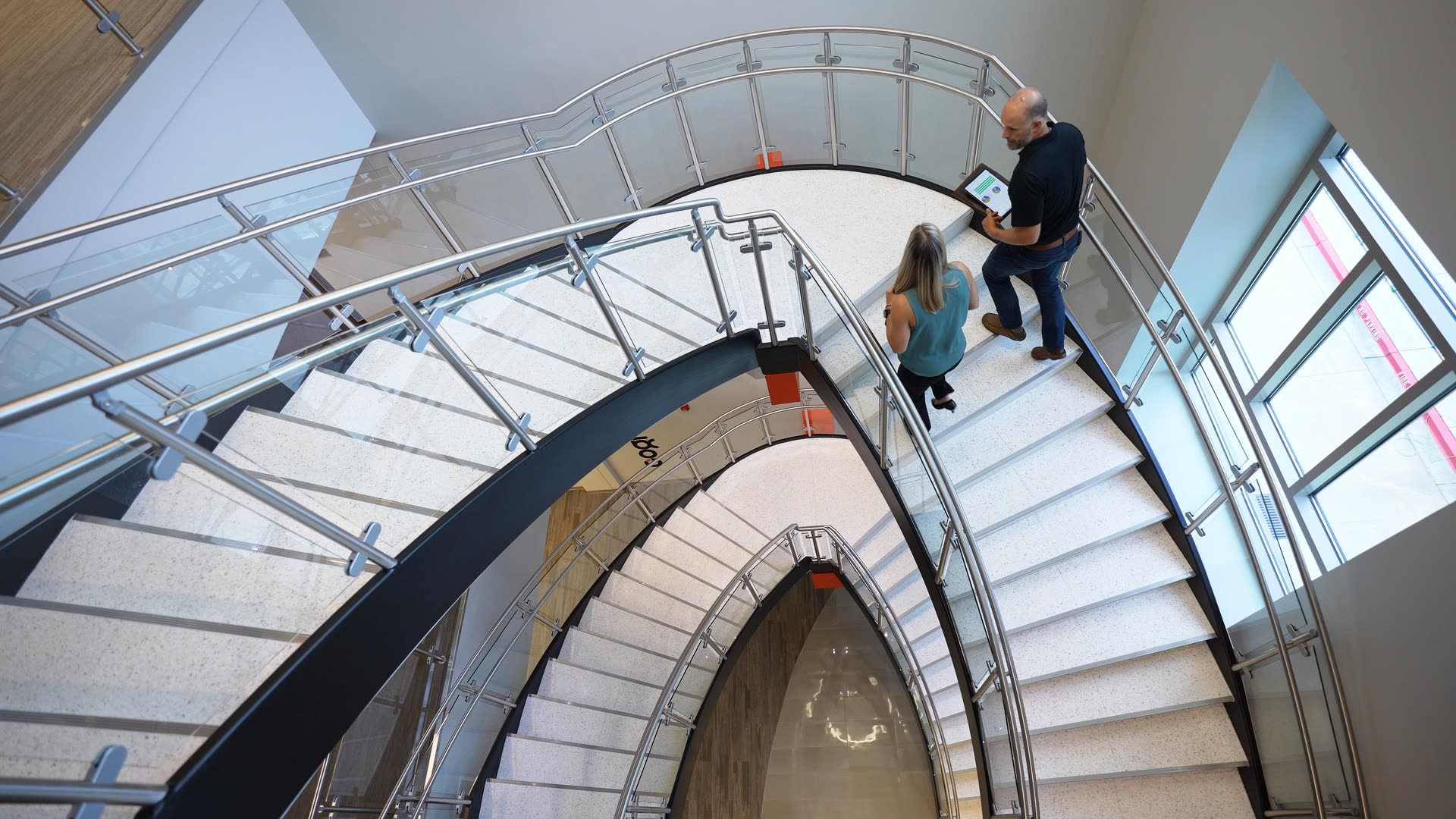 Two people conducting a facility walkthrough on a spiral staircase with a tablet